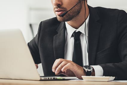 Man working on a laptop with a headset microphone.